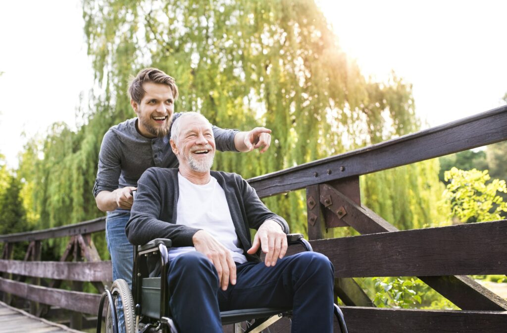 A caregiver pushes a resident in wheelchair across a bridge while they point and laugh at something in the distance