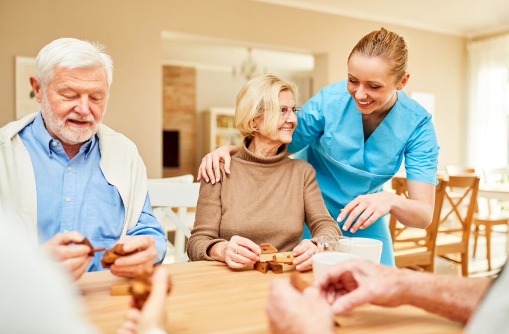 A senior attending group social time with others around a table being assisted by a nurse