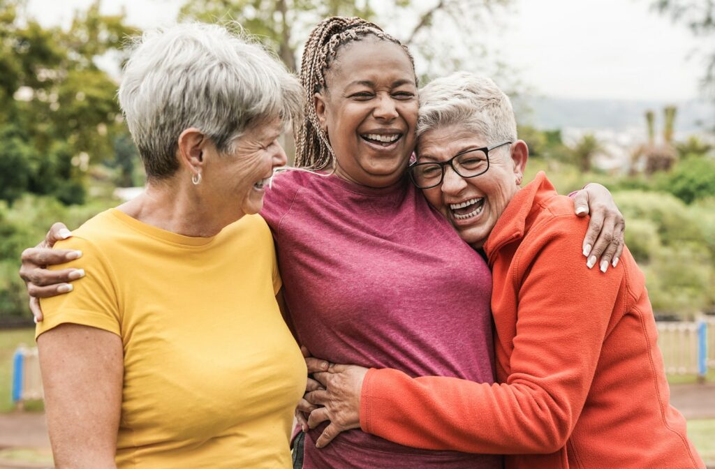 A group of three mature women embracing each other while laughing and enjoying the outdoors