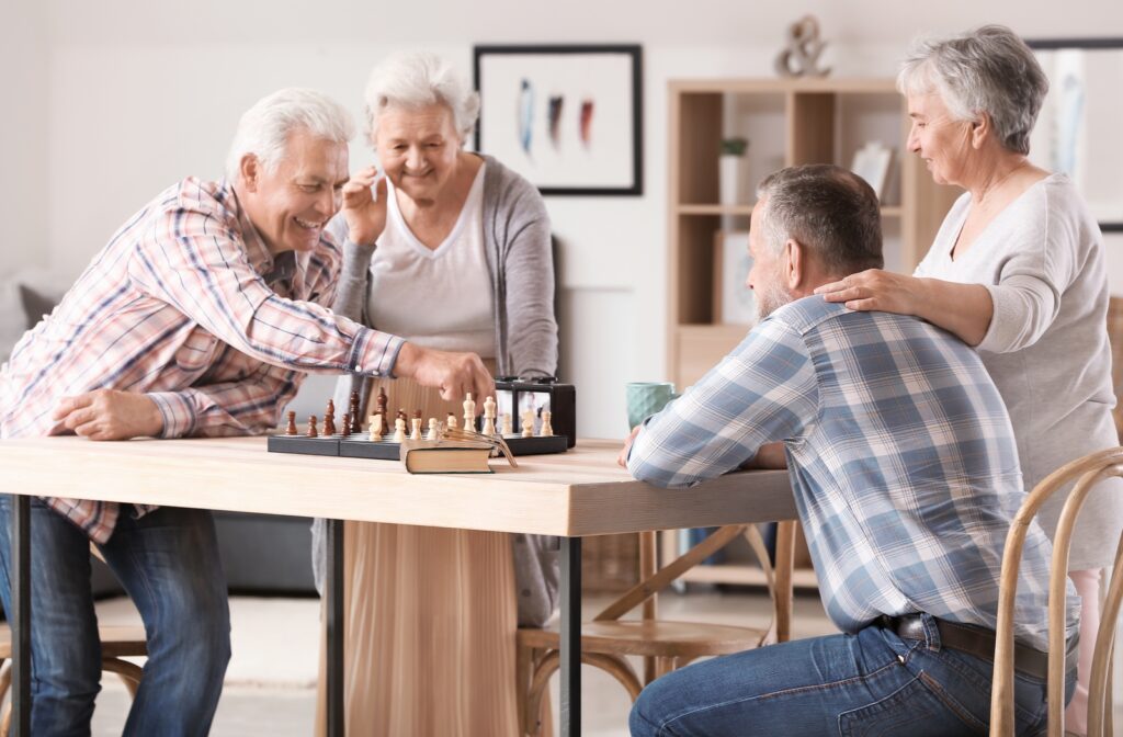 Four seniors standing around a table playing chess.