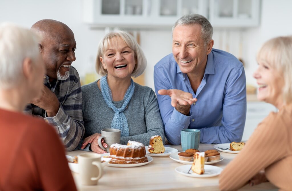 A group of seniors enjoying coffee and cake together while laughing.