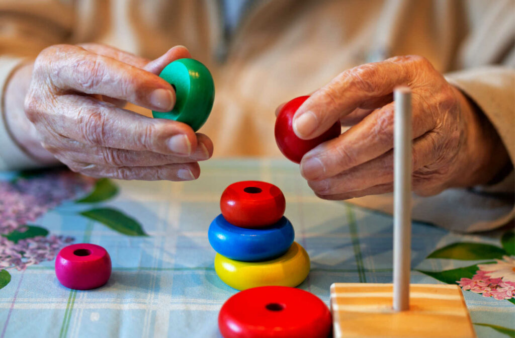 Close up photo of a mature adult's hands stacking colorful cylindrical wood blocks.