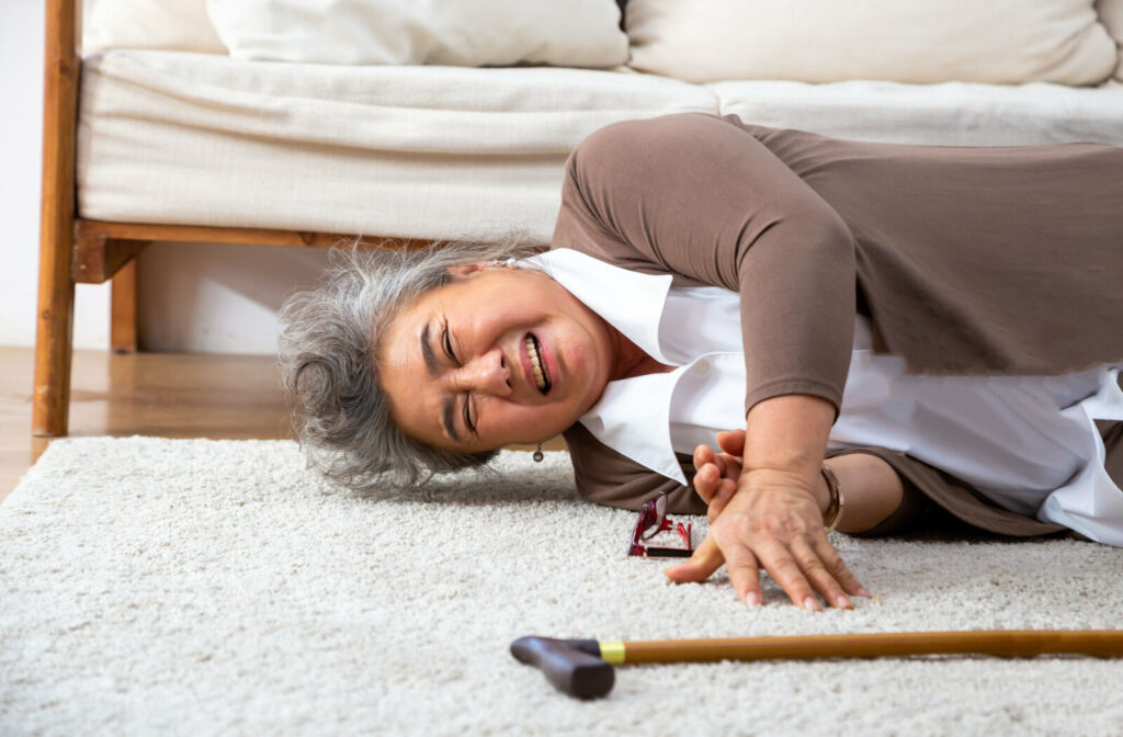 Senior woman is lying on the floor and reaching for a walking stick