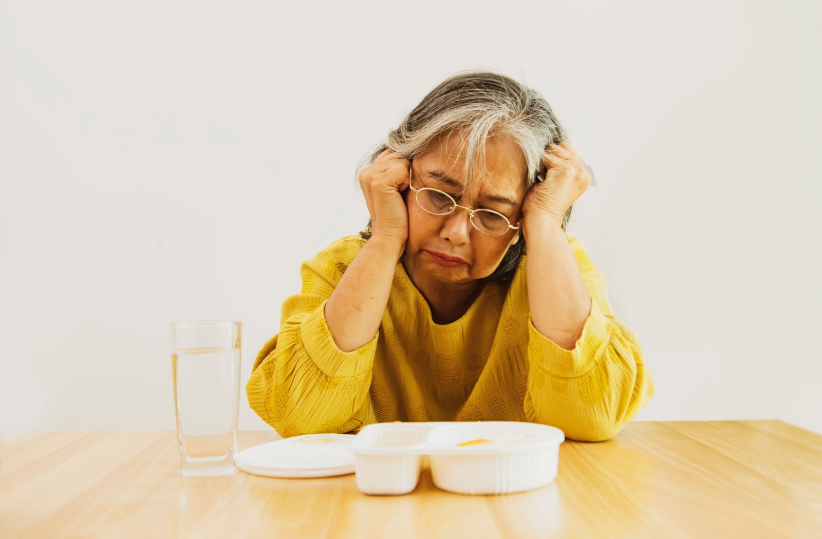 A senior woman holding her head while sitting at dinner table.