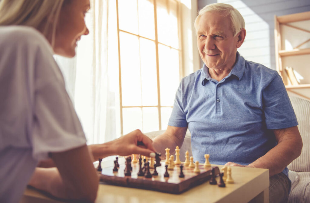 An elderly man with white hair playing chess with a young woman.