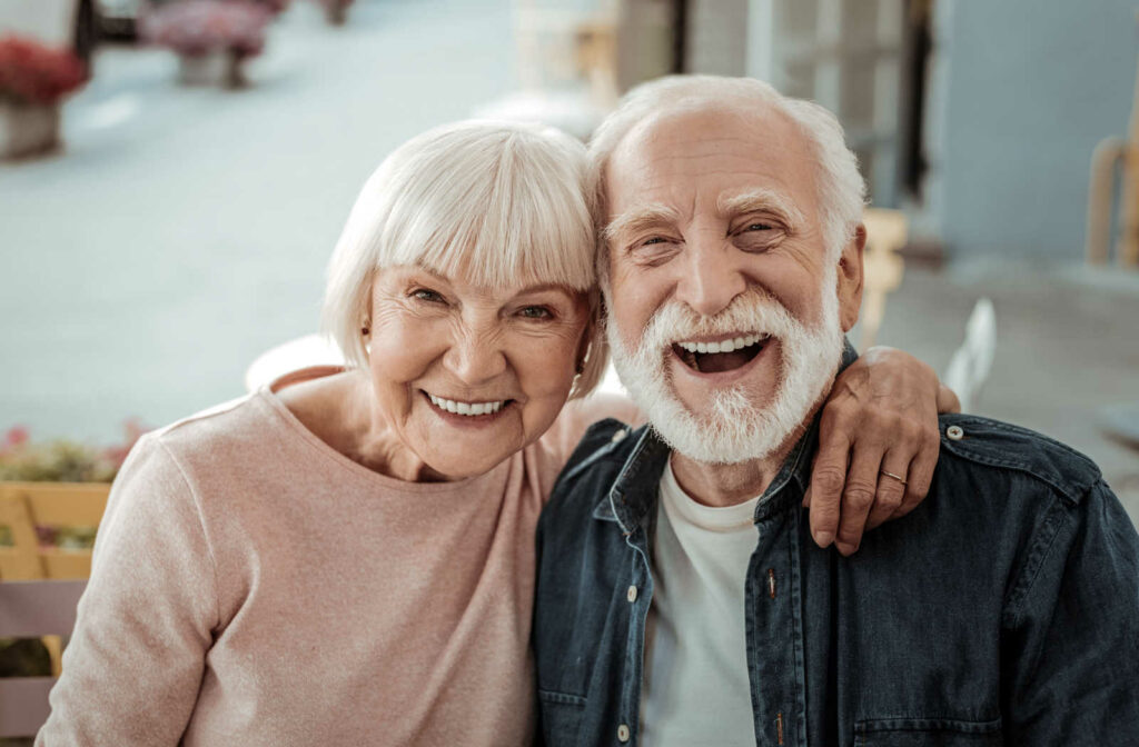A senior woman and a senior man with white hair smiling with wrinkles around their eyes and mouth.