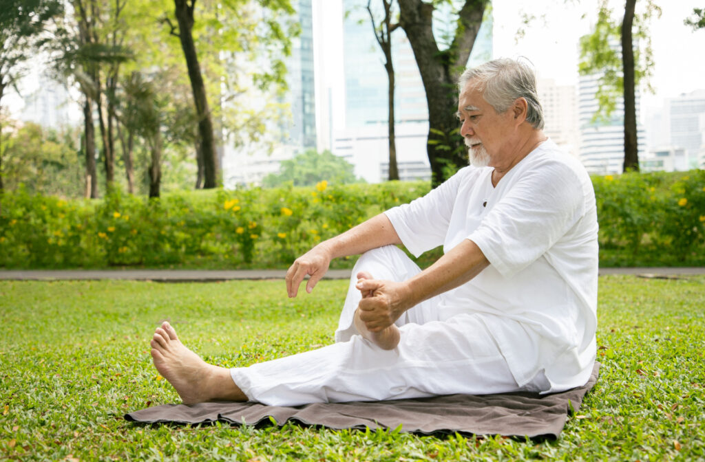 Mature man stretching on a blanket at the park.