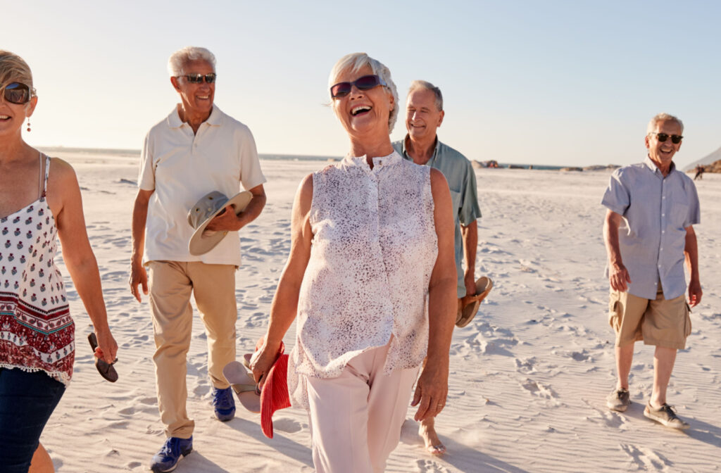 A group of smiling seniors walking together on a sunny beach.