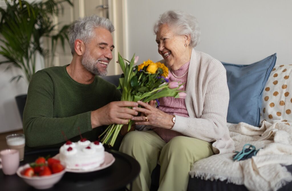 A middle-aged man giving a bouquet of flowers to his older adult mother during his visit.