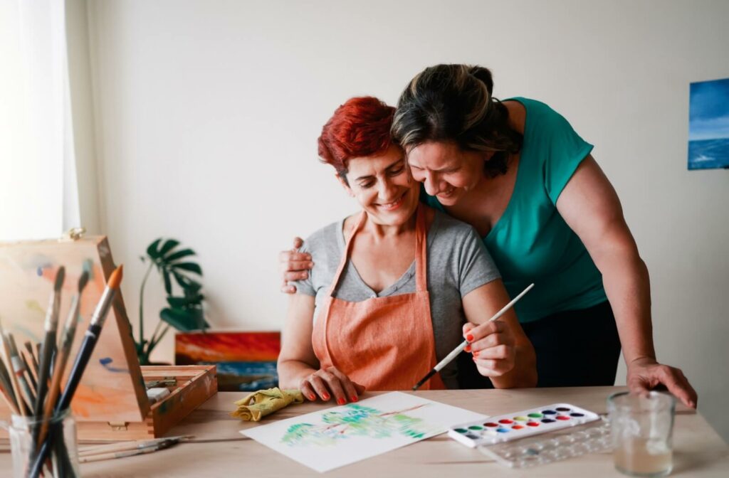 A senior couple express physical affection while engaging in a painting hobby in their independent living hom